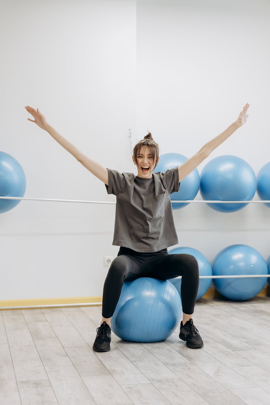 woman sitting on a yoga ball with arms raised